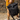 Person walking outdoors carrying a black roll-top backpack with a wide view of the stone-paved path and rustic stone wall in the background, wearing mustard corduroy shorts and beige sneakers in warm afternoon light.