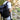 Person wearing a large black roll-top backpack while walking along a rocky riverside trail surrounded by nature and cliffs.
