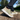 Close-up photograph of a person mid-stride on a gravel path, wearing two-tone olive green and beige canvas sneakers with thick white soles.