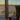 Olive-green 8000 Kicks backpack on an airport windowsill beside an unbranded coffee cup, with planes on the runway and a sunset in the background.