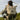 Person outdoors wearing a beige and black 8000Kicks backpack while hiking through grassy dunes, showcasing the minimalist weatherproof design in a natural setting.