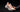 Hand holding a light pink running shoe with a knit upper and thick white sole against a dark background.