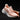 Hand holding a light pink running shoe with a knit upper and thick white sole against a dark background.