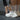 Person adjusting white 8000Kicks weatherproof hemp sneakers on a dark gym floor