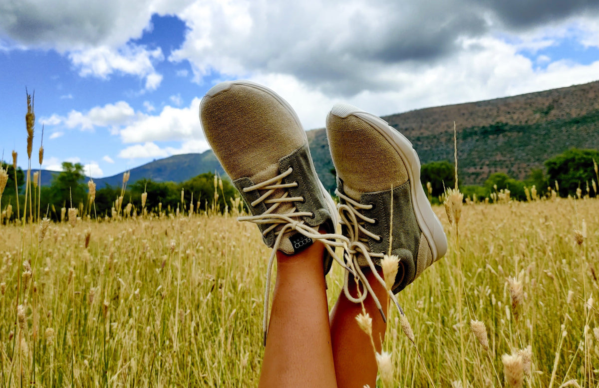 A person's legs raised in a grassy field under a cloudy blue sky, wearing the explorer v2