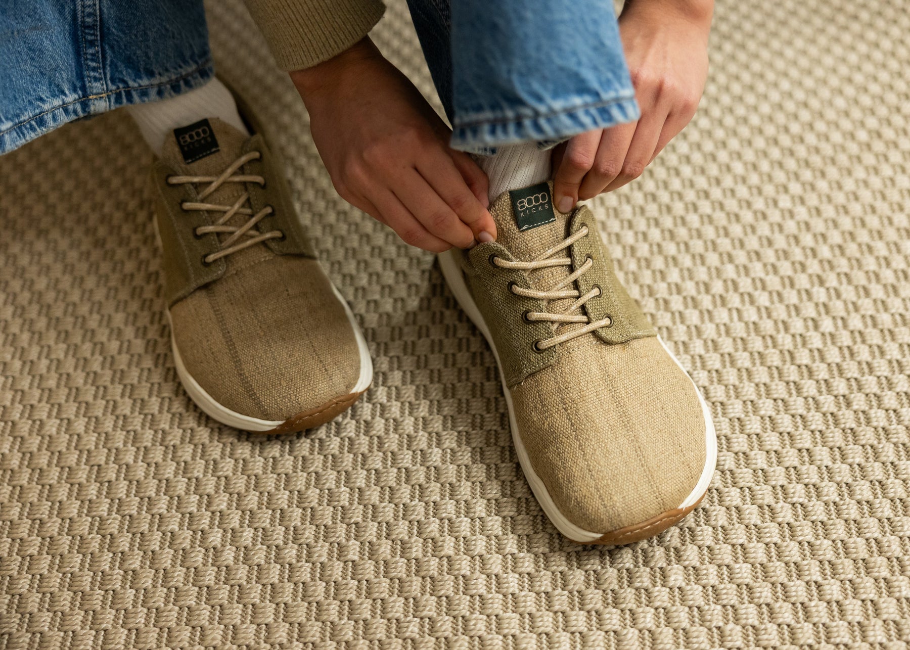 Person tying the laces of beige sneakers on a textured carpet